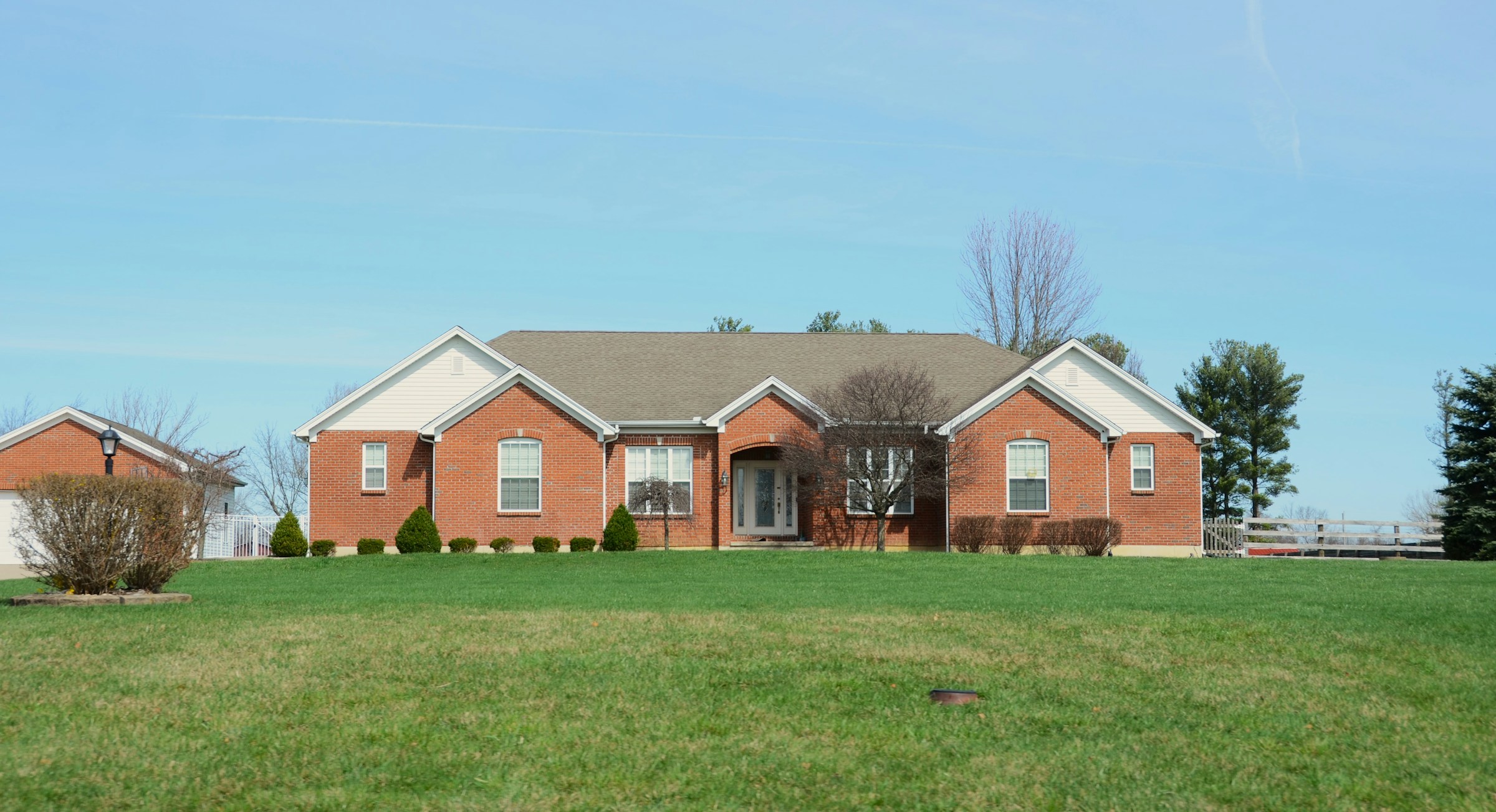 Traditional brick ranch home with white painted gables and trim, lawn, and trees
